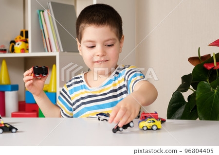 A preschool child plays with toy cars sitting at a table at home. 96804405