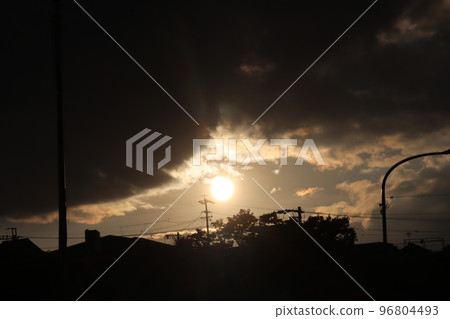 您可以看到在雲層和街道景觀之間以黑色輪廓在天空中照耀著傍晚橙色的太陽的風景 您可以看到在雲層和街道景觀之間以黑色輪廓在天空中照耀著傍晚橙色的太陽的風景 96804493