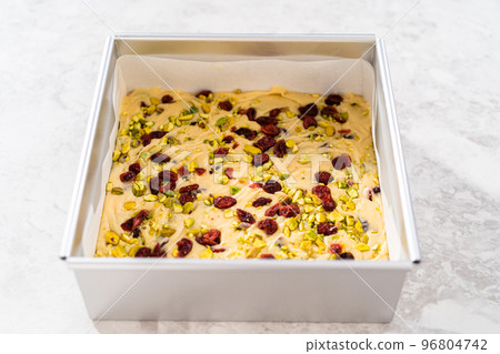 Removing cranberry pistachio fudge from a square cheesecake pan lined with parchment. 96804742