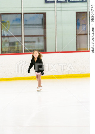 Little girl practicing figure skating on an indoor ice skating rink. 96804774