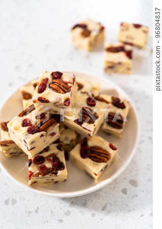 Homemade white chocolate cranberry pecan fudge pieces on a white ceramic plate. 96804837