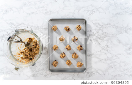 Flat lay. Scooping cookie dough with dough scoop into a baking sheet lined with parchment paper to bake soft oatmeal raisin walnut cookies. 96804895