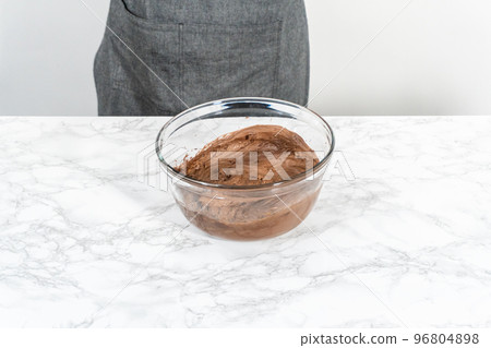 Mixing store-bought chocolate frosting in a mixing glass bowl with a hand mixer. 96804898