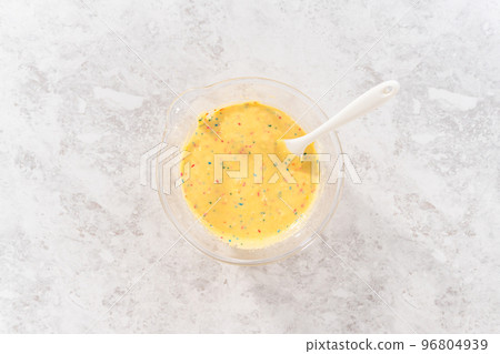 Flat lay. Mixing ingredients in a glass mixing bowl to bake funfettti bundt cake. 96804939