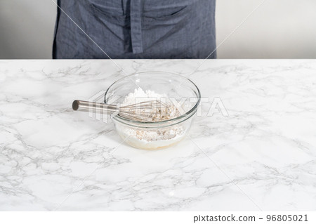 Lemon glaze. Mixing ingredients with a hand whisk in a glass mixing bowl to make lemon glaze. 96805021