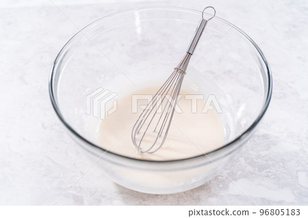 Mixing ingredients in a glass mixing bowl to prepare the white glaze. 96805183