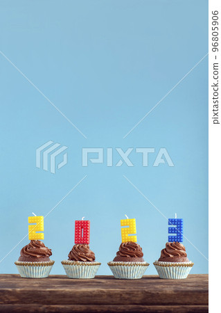 Happy New Year 2023 theme. Homemade chocolate cupcakes with 2023 number colorful candle on wooden table. Vertical frame, blue background. 96805906