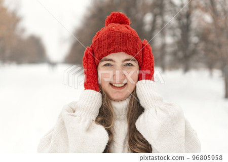 Portrait of laughing beautiful young woman in knitted red hat and mittens. Woman walking in winter park 96805958