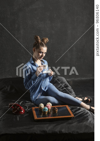 Extraordinary girl in blue shirt drinks coffee and eats muffins on black background in studio. Cupcakes on black tray 96806140
