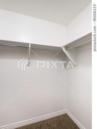 Vertical White shelves with wooden brackets and metal rods inside a walk in closet Vertical White shelves with wooden brackets and metal rods inside a walk in closet 96806224