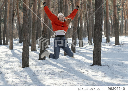 Walk through the winter wood on sunny day. Happy young woman in snowy forest jumps high 96806240