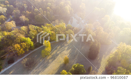 Aerial flying over trees with yellow leaves, meadow, dirt road with morning mist an autumn sunny morning in park. Bright sunlight, shining sunbeams rays, sun overexposure. Beautiful natural background Aerial flying over trees with yellow leaves, meadow, dirt road with morning mist an autumn sunny morning in park. Bright sunlight, shining sunbeams rays, sun overexposure. Beautiful natural background 96810087