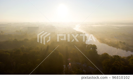 Forest park trees, river and many high-rise buildings in city in early morning at dawn in summer. Brightly shining sun, clear cloudless sky and morning mist Sunbeams and shadows Aerial drone landscape Forest park trees, river and many high-rise buildings in city in early morning at dawn in summer. Brightly shining sun, clear cloudless sky and morning mist Sunbeams and shadows Aerial drone landscape 96810102