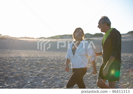 Cheerful man and woman smiling while walking along seashore 96811313