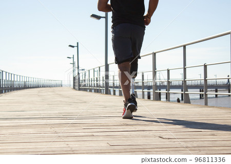 Back view of athlete with prosthetic leg jogging in morning Back view of athlete with prosthetic leg jogging in morning 96811336