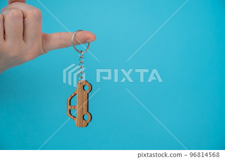 Woman's hand holding a wooden keychain in the shape of a car on a blue background. 96814568