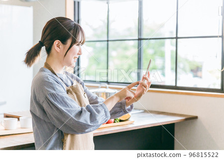 Asian woman using smartphone app in home kitchen/dining Asian woman using smartphone app in home kitchen/dining 96815522