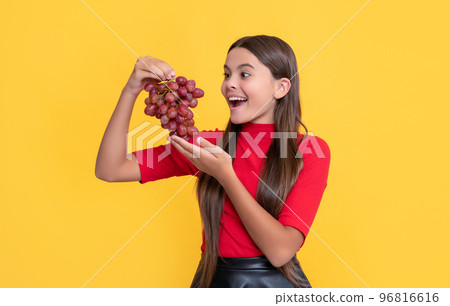 amazed positive child hold bunch of grapes on yellow background 96816616