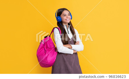 cheerful child in headphones with school backpack on yellow background 96816623