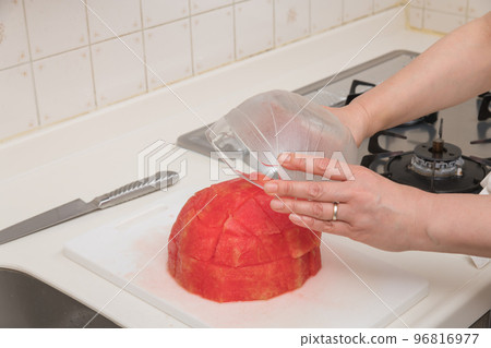 [A middle-aged housewife prepares cut watermelon, flipping the watermelon on the cutting board and transferring it to a bowl] 96816977