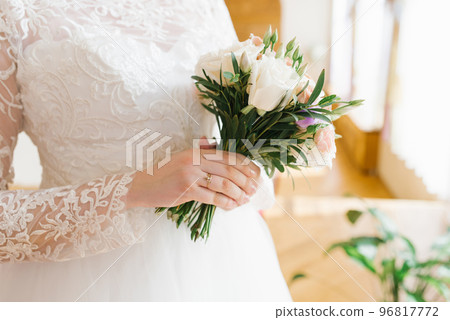 Delicate beautiful stylish bouquet in the hands of the bride. An engagement ring is worn on a hand at a wedding 96817772