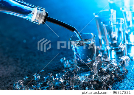 Vodka poured into a glass lit with blue backlight. 96817821