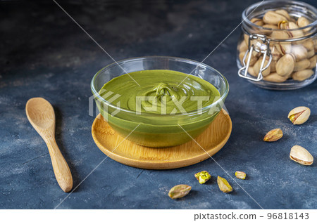 Pistachio spread cream in glass bowl, raw pistachios in jar, wooden tea spoon on dark stone background Pistachio spread cream in glass bowl, raw pistachios in jar, wooden tea spoon on dark stone background 96818143