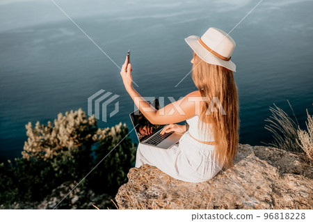 Digital nomad, Business woman working on laptop by the sea. Pretty lady typing on computer by the sea at sunset, makes a business transaction online from a distance. Freelance, remote work on vacation Digital nomad, Business woman working on laptop by the sea. Pretty lady typing on computer by the sea at sunset, makes a business transaction online from a distance. Freelance, remote work on vacation 96818228