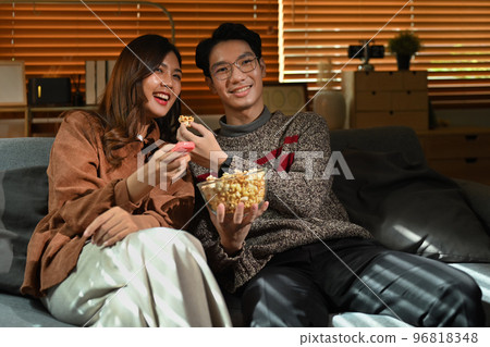 Couple watching moving, television streaming services while sitting on a Couch in the living room Couple watching moving, television streaming services while sitting on a Couch in the living room 96818348