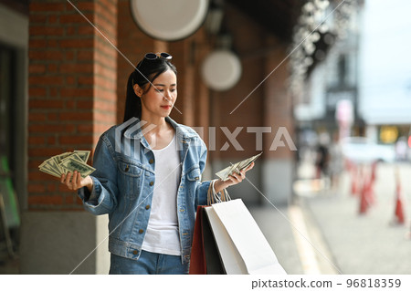 Photo of trendy woman with fan of money and colorful shopping bags. Shopping and holiday vacation activity lifestyle concept Photo of trendy woman with fan of money and colorful shopping bags. Shopping and holiday vacation activity lifestyle concept 96818359