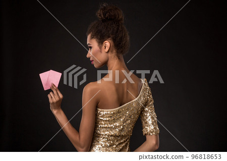 Woman winning - Young woman in a classy gold dress holding two cards, a poker of aces card combination. 96818653