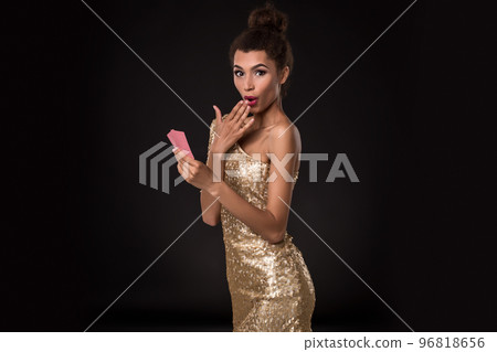 Woman winning - Young woman in a classy gold dress holding two cards, a poker of aces card combination. Emotions 96818656