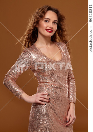 Portrait of young caucasian female in golden cocktail dress looking into the camera on brown background Portrait of young caucasian female in golden cocktail dress looking into the camera on brown background 96818811