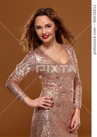 Portrait of young caucasian female in golden cocktail dress looking into the camera on brown background Portrait of young caucasian female in golden cocktail dress looking into the camera on brown background 96818812