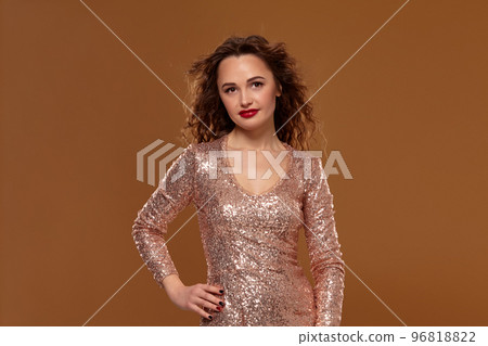 Portrait of young caucasian female in golden cocktail dress looking into the camera on brown background 96818822