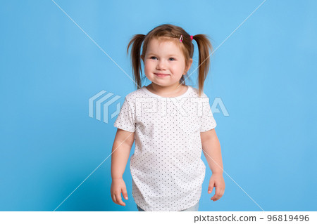 Funny kid in white T-shirt on blue background. Little pretty girl isolated on blue background. Copy space for text. Funny kid in white T-shirt on blue background. Little pretty girl isolated on blue background. Copy space for text. 96819496