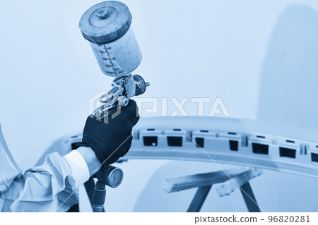 Mechanic painting bumper of a car with sprayer in painting booth in repair auto service Mechanic painting bumper of a car with sprayer in painting booth in repair auto service 96820281