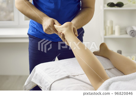 Male masseur in health clinic or massage parlor does hand massage of young woman's feet. Male masseur in health clinic or massage parlor does hand massage of young woman's feet. 96820846