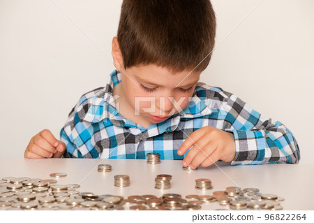 A preschool boy in a plaid shirt counts coins, builds towers. Financial literacy for children. 96822264