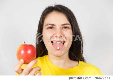 A woman holds in her hand an apple, a white tablet of vitamins or dietary supplements on the tongue. A woman holds in her hand an apple, a white tablet of vitamins or dietary supplements on the tongue. 96822344