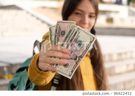 A teenage girl shows a lot of dollar bills and smiles. 96822452