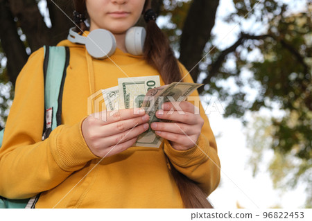 A teenage girl in headphones counts dollar bills, pocket money 96822453