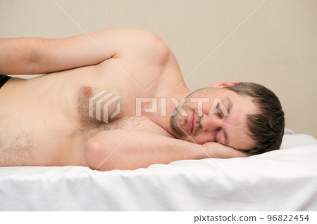 A man lies on a mattress without a pillow on his side with his arm placed under his head 96822454