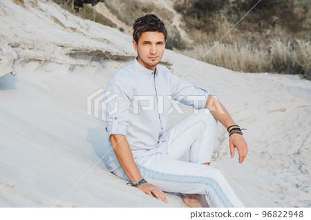 Young handsome man in light clothing sits in the desert. Concept of freedom relaxation. Place for text or advertising Young handsome man in light clothing sits in the desert. Concept of freedom relaxation. Place for text or advertising 96822948