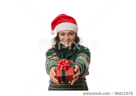 Latin American pretty woman wearing green Xmas patterned sweater and Santa hat, holding a cute gift box with Christmas surprise, cutely smiling looking at camera, isolated over white background 96822978