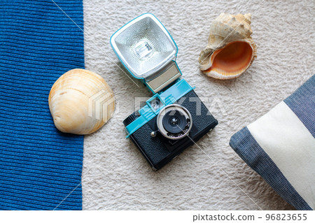 Plastic film camera, sea shells and stripped cushion on a textured textile background Plastic film camera, sea shells and stripped cushion on a textured textile background 96823655