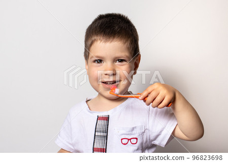 A little boy holds an orange toothbrush with toothpaste. The child brushes his teeth, prevention of tooth decay A little boy holds an orange toothbrush with toothpaste. The child brushes his teeth, prevention of tooth decay 96823698