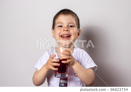 A little boy is drinking cherry juice from a glass. Juices and vitamins in the diet of children. A little boy is drinking cherry juice from a glass. Juices and vitamins in the diet of children. 96823734