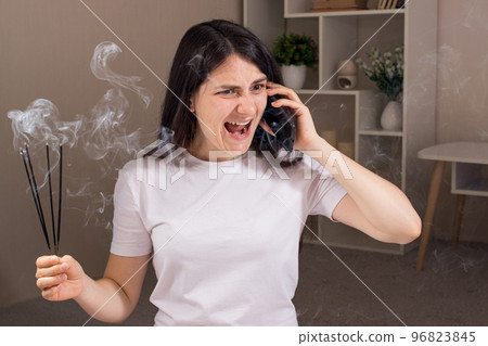 A stressed businesswoman is on the phone and nervous, shouts, calms down with aromatherapy and aromatic sticks. A stressed businesswoman is on the phone and nervous, shouts, calms down with aromatherapy and aromatic sticks. 96823845