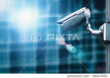 External security camera on pole in front of glass building wall 96824008